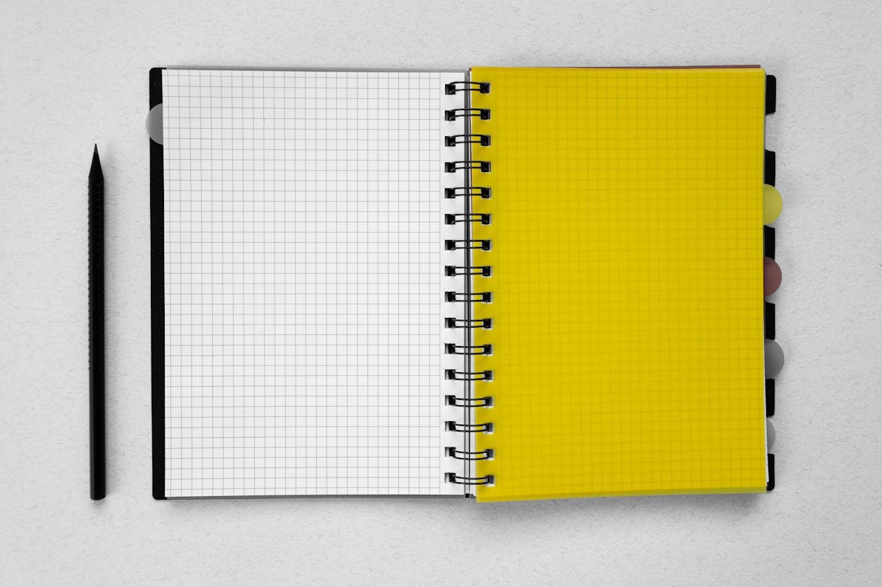 Flat lay of a spiral notebook with graphing paper and a pencil on a neutral background.